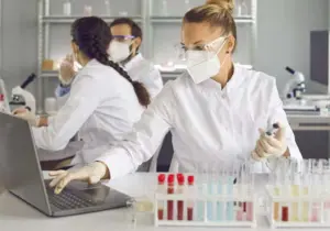Photo of a lab scientist holding a pipette and working on the computer