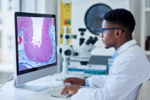 Photo of a pathology lab technician looking at a slide on a computer screen.